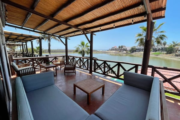Rooftop pool deck with white lounge chairs, gray umbrellas, and blue swimming pool overlooking coastal city and sea.